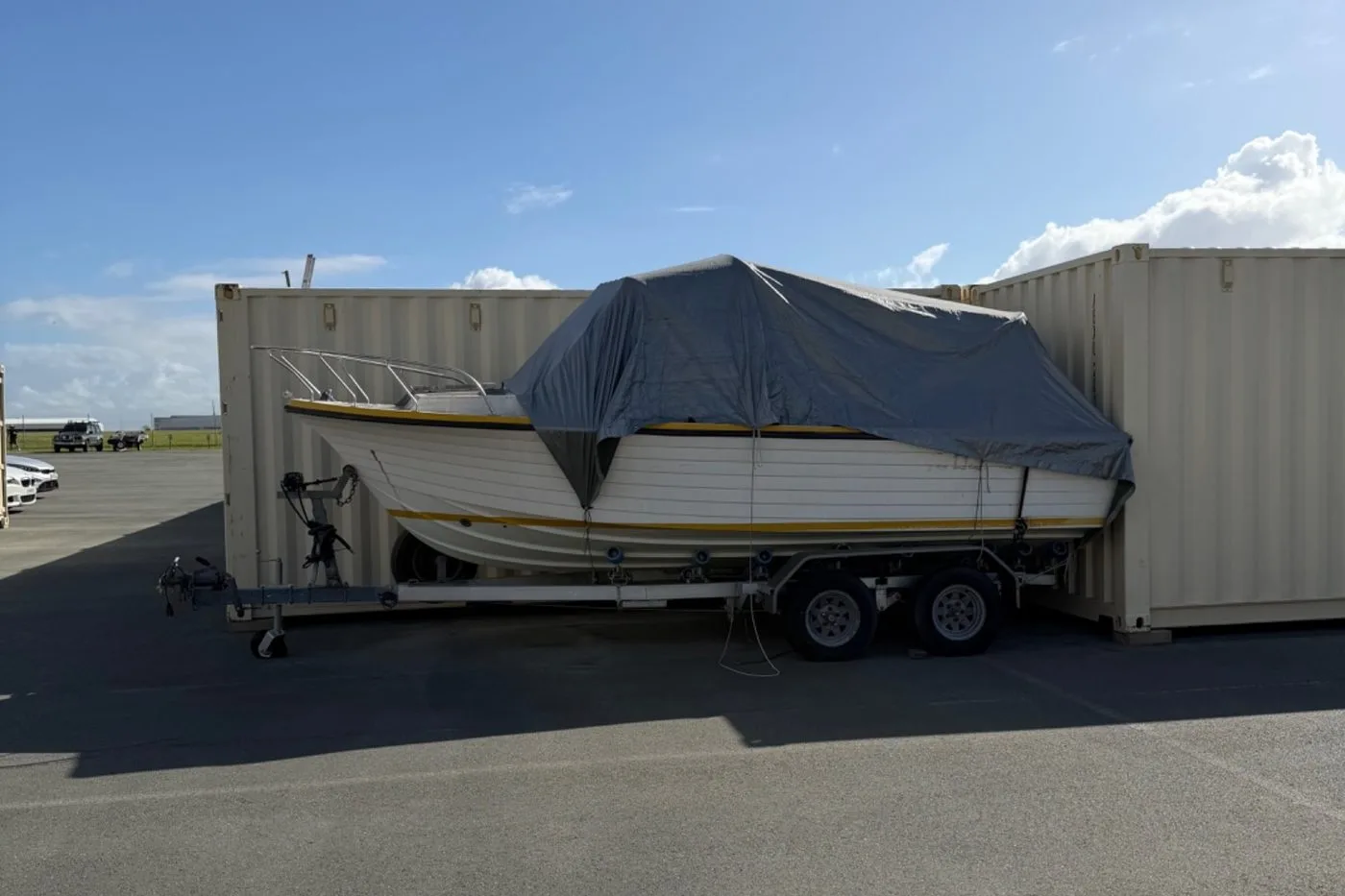 Covered boat on a tandem trailer stored beside shipping containers at Storage Land, Archerfield Brisbane